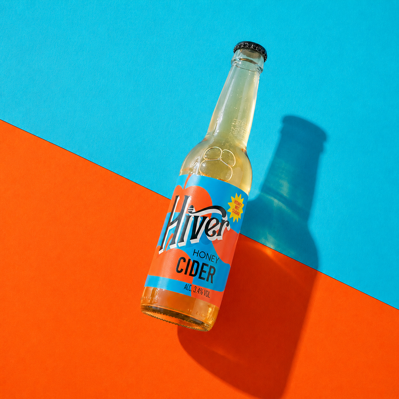 Bottle of Hiver Honey Cider standing on a bold blue and orange background