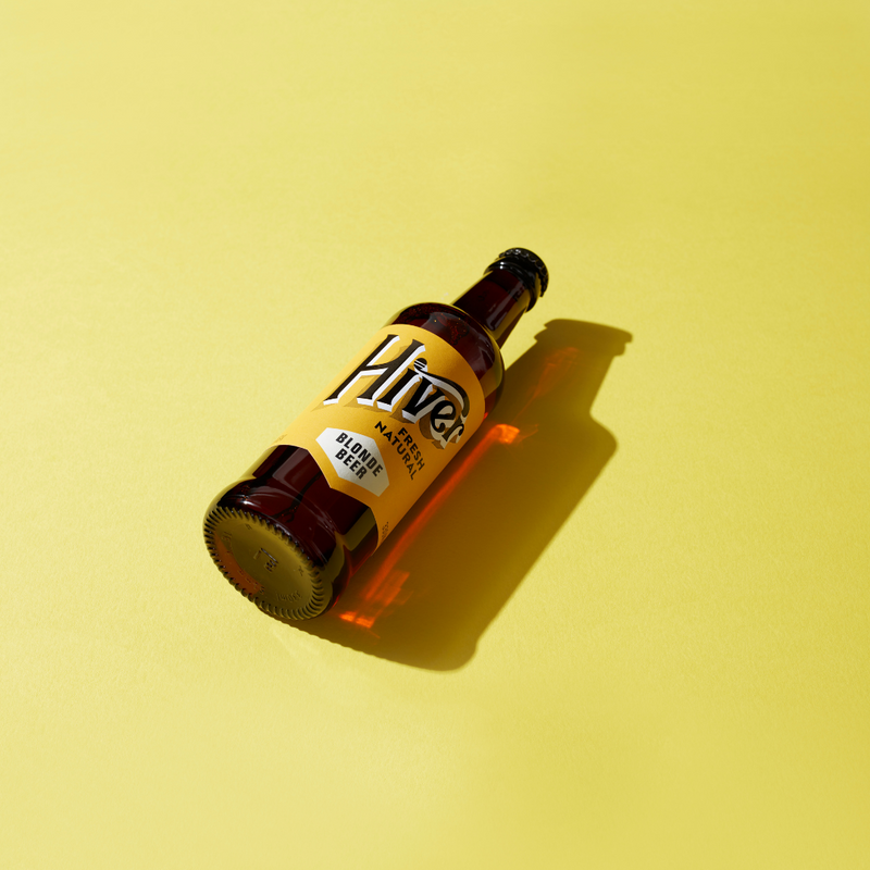 Bottle of Hiver Blonde honey beer lying on a yellow background with dramatic shadow